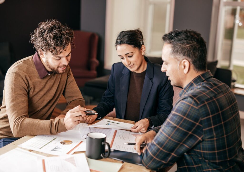 Three individuals engaged in discussion at a table, reviewing papers and a phone related to commercial mortgages.