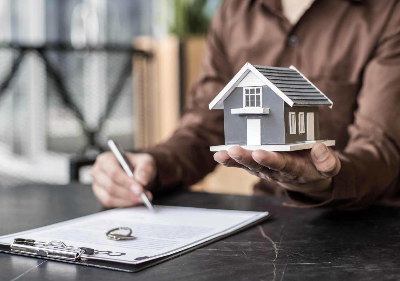 A man holds a house model on paper, accompanied by a pen, symbolizing the concept of second mortgages